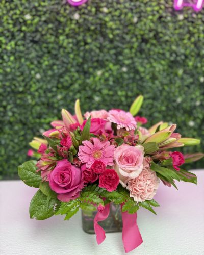 <p>A lush low bouquet of pink roses, gerbera, carnations alstromeria and lily buds in a glass vase with ribbon</p>