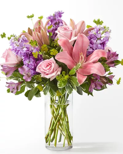 <p>full rounded bouquet of pink lilies, soft pink roses, alstroemeria and purple accents in a clear vase</p>