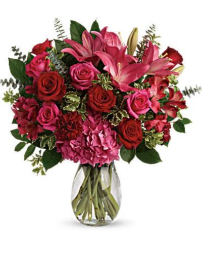 <p>Deep pinks and rich reds adorned with fresh greens in a glass vase</p>