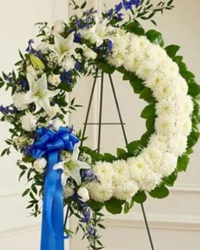 With blue flowers that symbolize truth and white blooms that signify honor, this standing wreath arrangement beautifully reflects the love and sympathy that is in your heart. Exquisitely crafted by our expert florists, it features a gathering of fresh blue delphinium, white roses, lilies, mums, carnations, monte casino and more accented by variegated pittosporum, ruscus and salal. Appropriate for family, friends and business associates to send directly to the funeral home.
