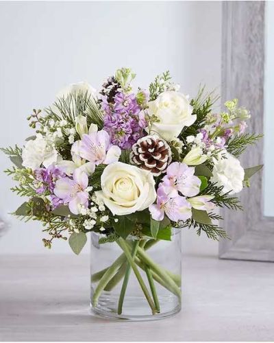 We’ve captured the peaceful beauty of winter in our lovely bouquet. A new seasonal version of our best seller, it’s loosely gathered with soothing lavender & white blooms, cascading greenery all around and pinecone accents for a rustic touch. A truly wonderful way to express your sentiments this time of year.
<ul>
<li>All-around arrangement with white roses and carnations; lavender Peruvian lilies (alstroemeria) and stock; accented with baby’s breath, seeded eucalyptus, pinecone picks and assorted Christmas greenery</li>
<li>Artistically designed a clear glass cylinder vase</li>
<li>Large arrangement measures approximately 15"H x 13"W</li>
<li>Medium arrangement measures approximately 13"H x 12"W</li>
<li>Small arrangement measures approximately 12"H x 9"W</li>
<li>Our florists select the freshest flowers available, so colors, varieties and container may vary due to local availability</li>
<li>To ensure lasting beauty, Peruvian lilies may arrive in bud form and will fully bloom over the next few days</li>
</ul>