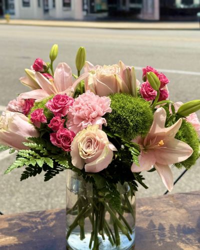Pink roses, lilies, spray roses, carnations and greens designed in a glass cylinder.